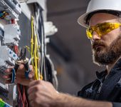 Male electrician at the checkout counter on a blurred background of a switchboard.